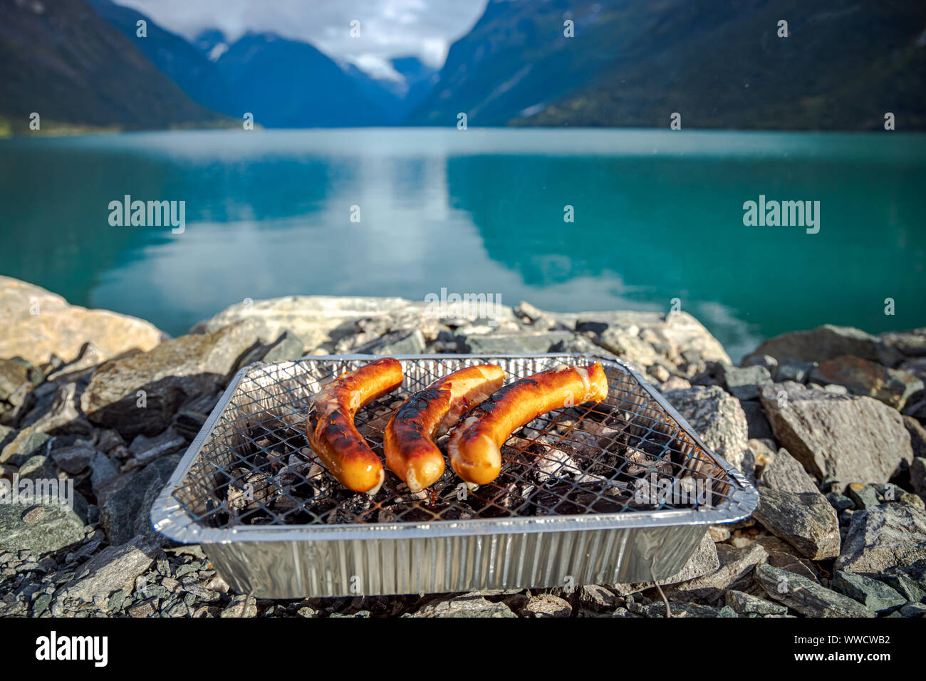 Grilling sausages on disposable barbecue grid. Beautiful Nature Norway natural landscape. Stock Photo