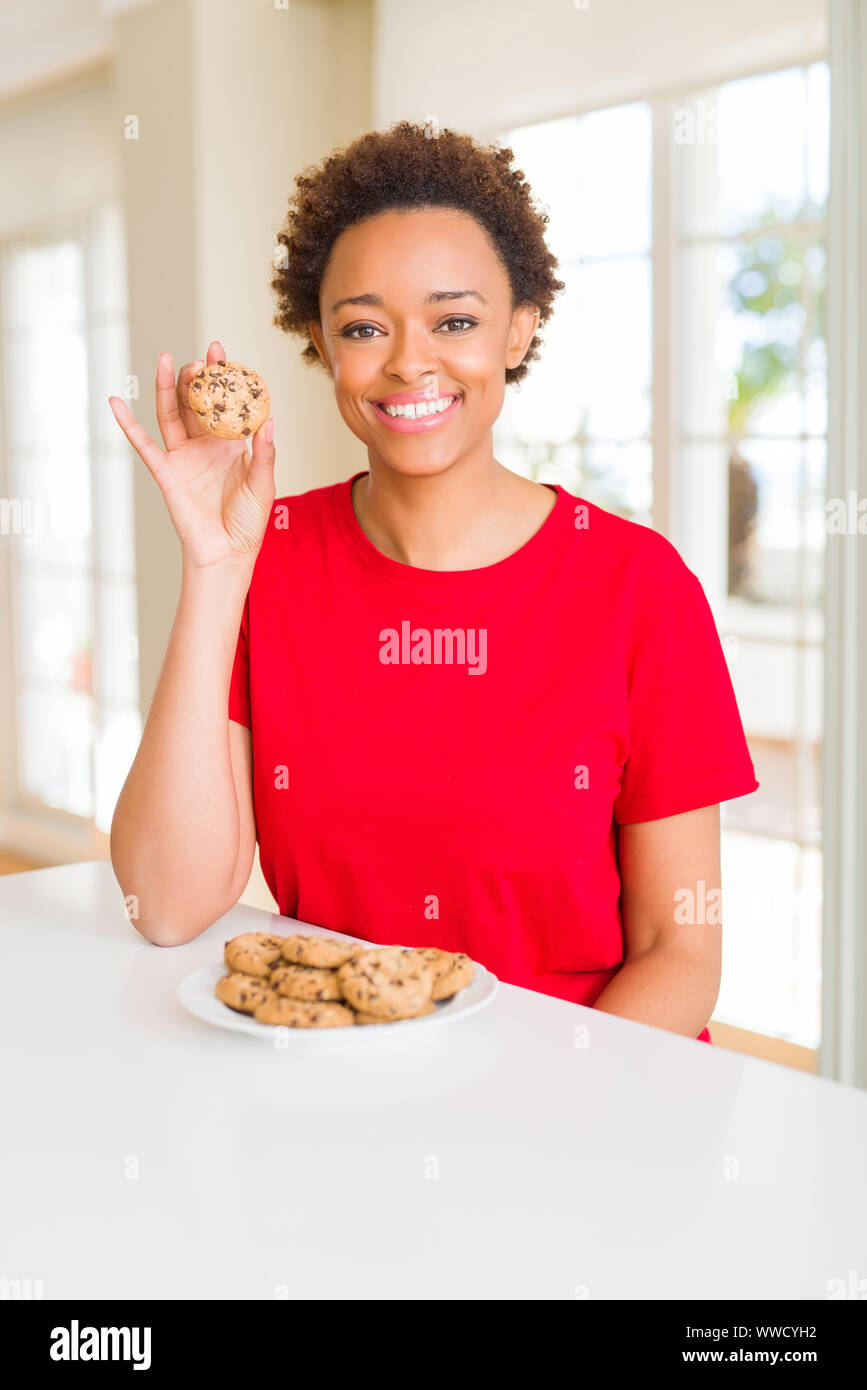 Young african american woman eating chocolate chips cookies with a happy face standing and smiling with a confident smile showing teeth Stock Photo