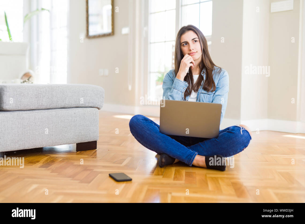 Beautiful young woman sitting on the floor with crossed legs using ...