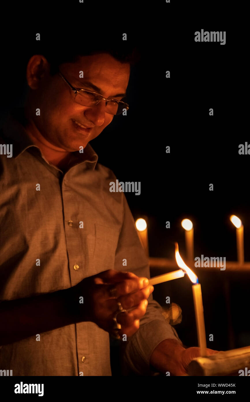 Indian Man lighting up candles at night on Diwali kali puja or pooja - an Indian Hindu festival of lights. Stock Photo