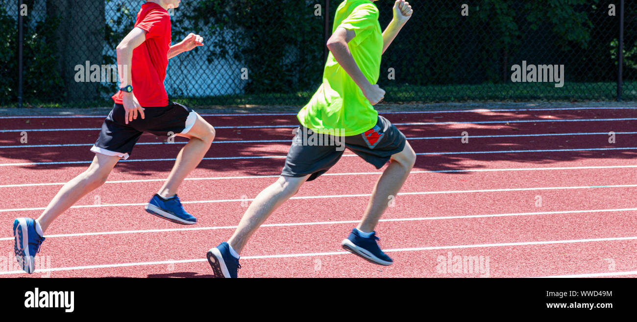 Two young boys running fast clockwise on a red track during a track and field running camp. Stock Photo