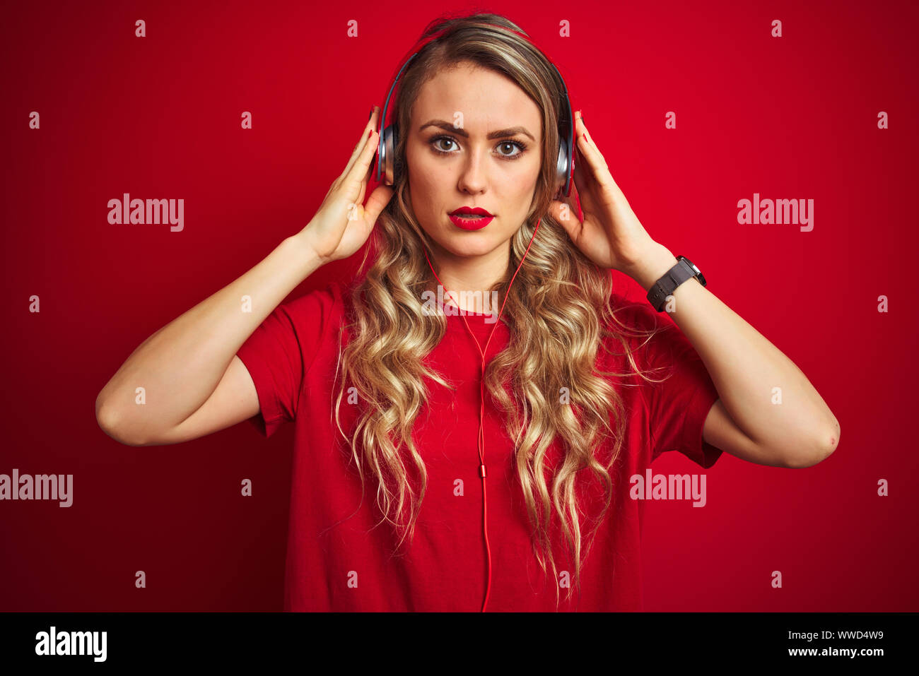 Young beautiful woman wearing headphones over red isolated background ...