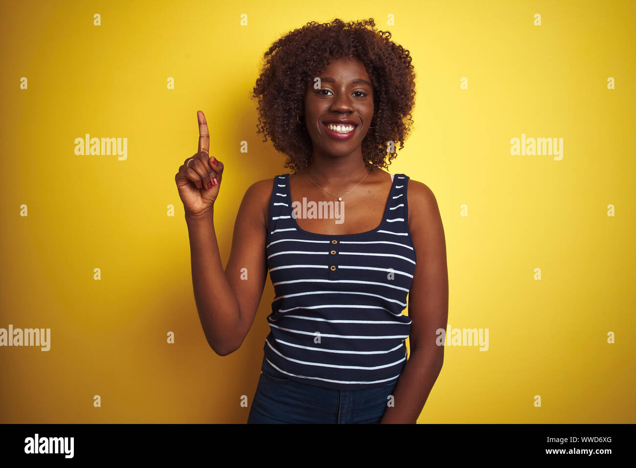 Young african afro woman wearing striped t-shirt over isolated yellow ...