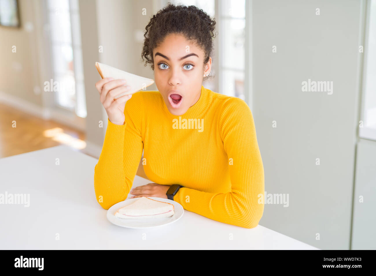 Young african american woman eating a sandwich as healthy snack scared