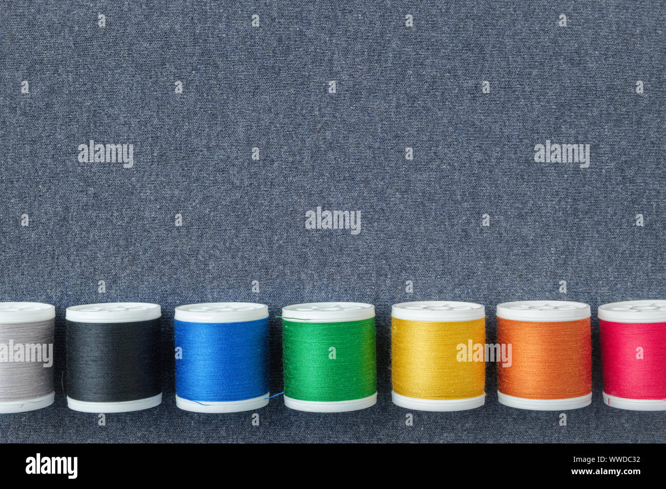 Row of spools of multicolored threads on sewing cloth. View from above. Copy space for text. Stock Photo