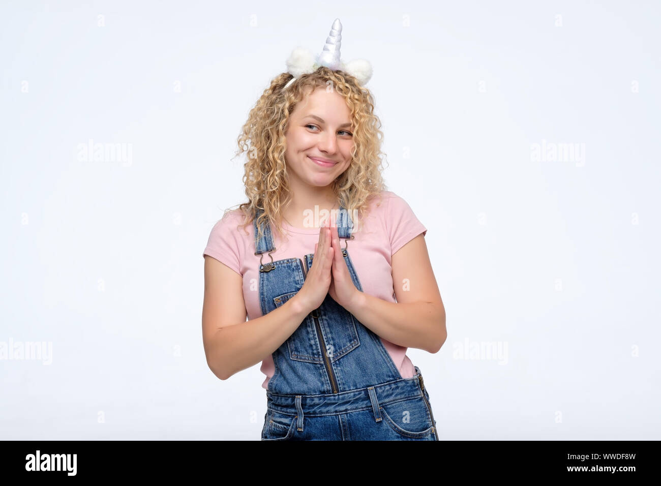 Cunning woman with curly hair and unicorn horn looking aside indenting to realize tricky plan. Attractive female having sly expression. Studio shot Stock Photo