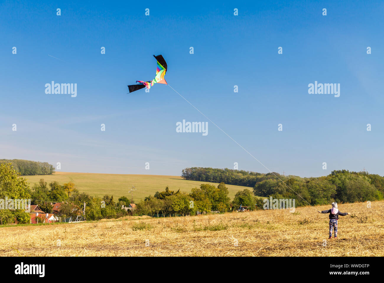 Brightly colored kite in the wind with a blue sky and a small child in ...