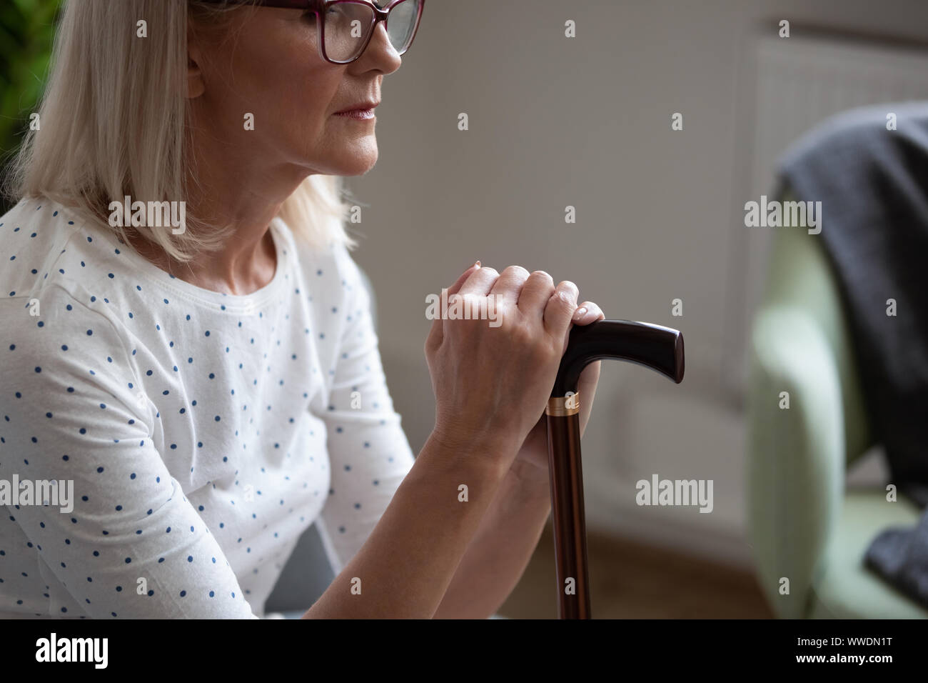 Cropped upset mature woman in glasses holding cane, sitting alone Stock Photo