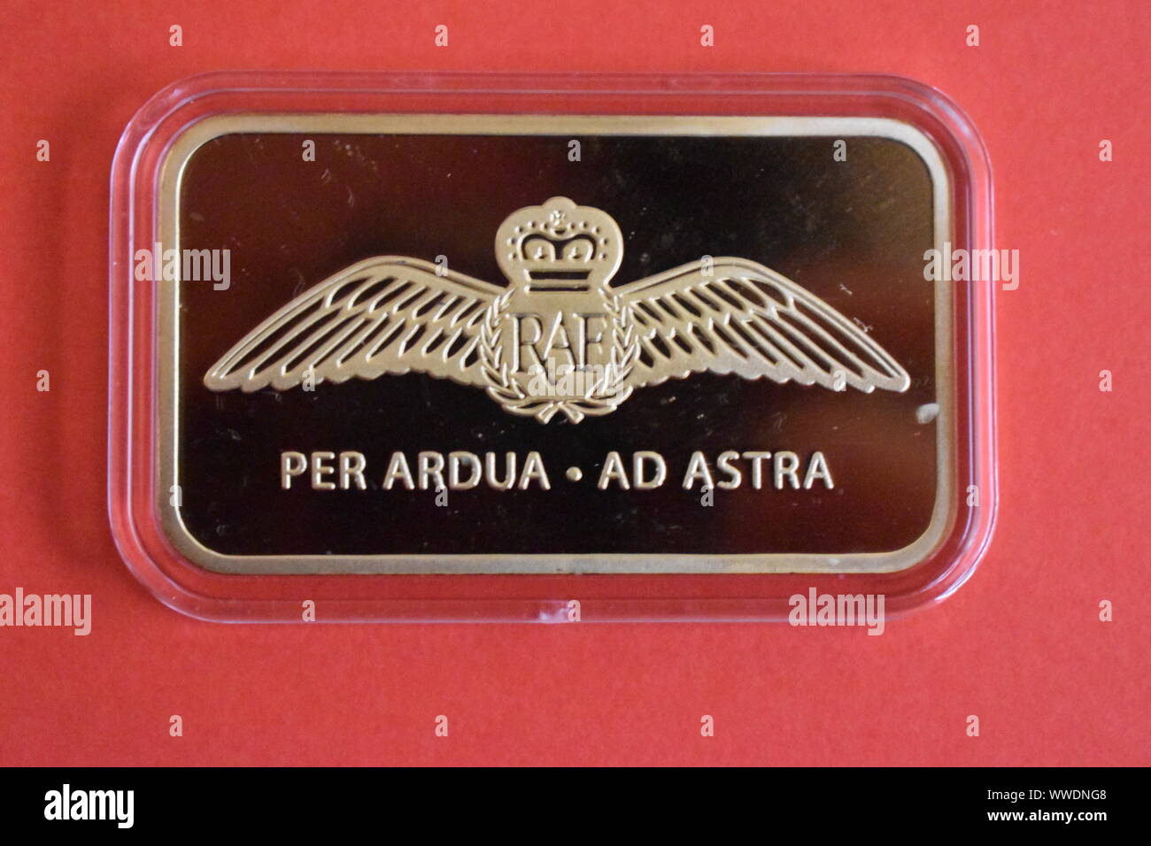 Reverse side of the new Red Arrows 24 carat Gold-Plated Ingot 2019 with a bird and the words, PER ARDUA . AD ASTRA on it. With a pink background. Stock Photo