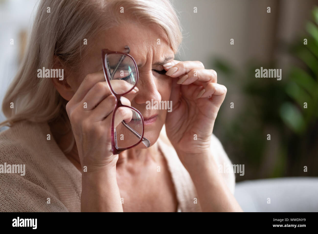 Tired older woman taking off glasses, feeling eye strain Stock Photo