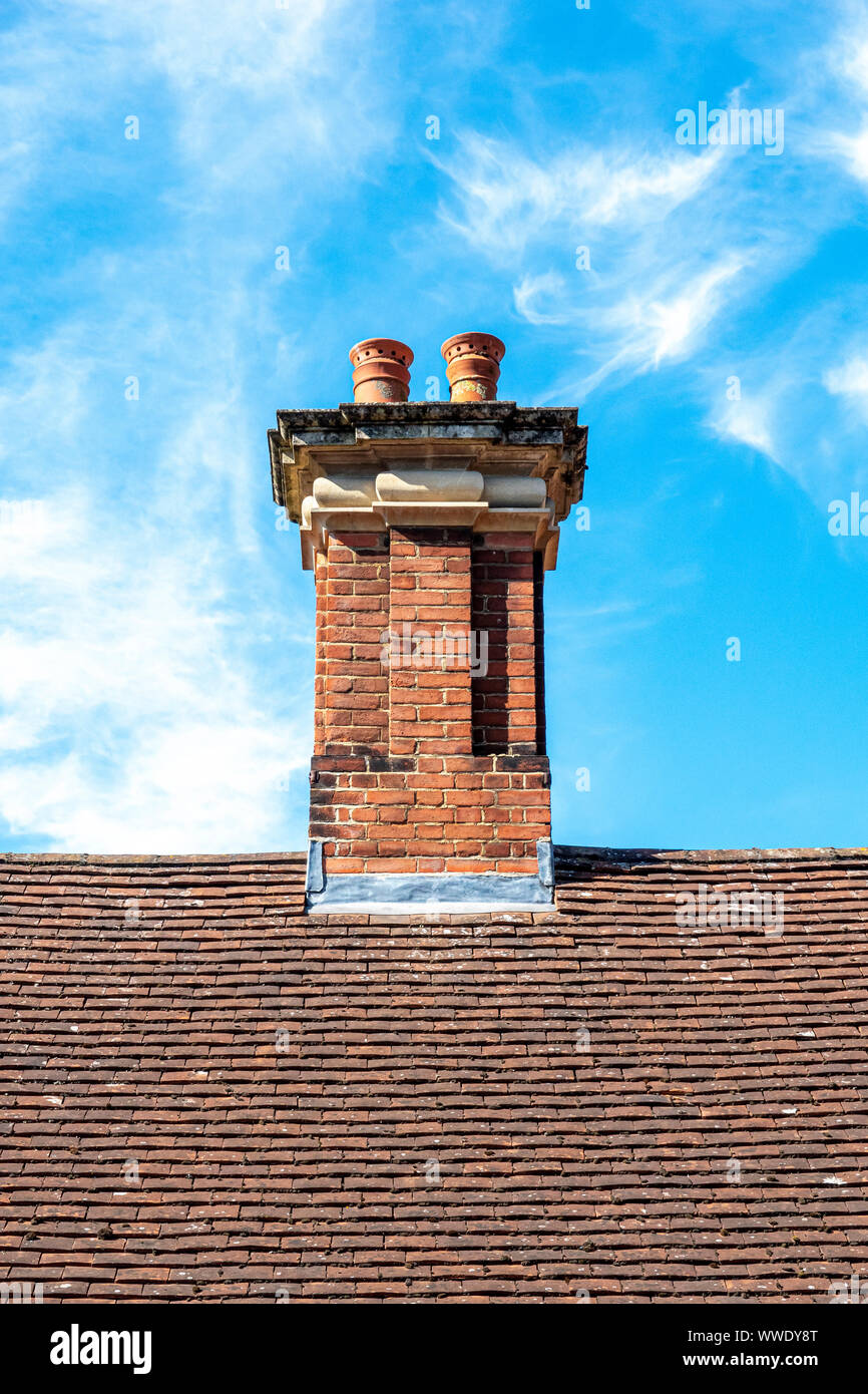 Brick chimney on top of clay tile roof against blue sky Stock Photo