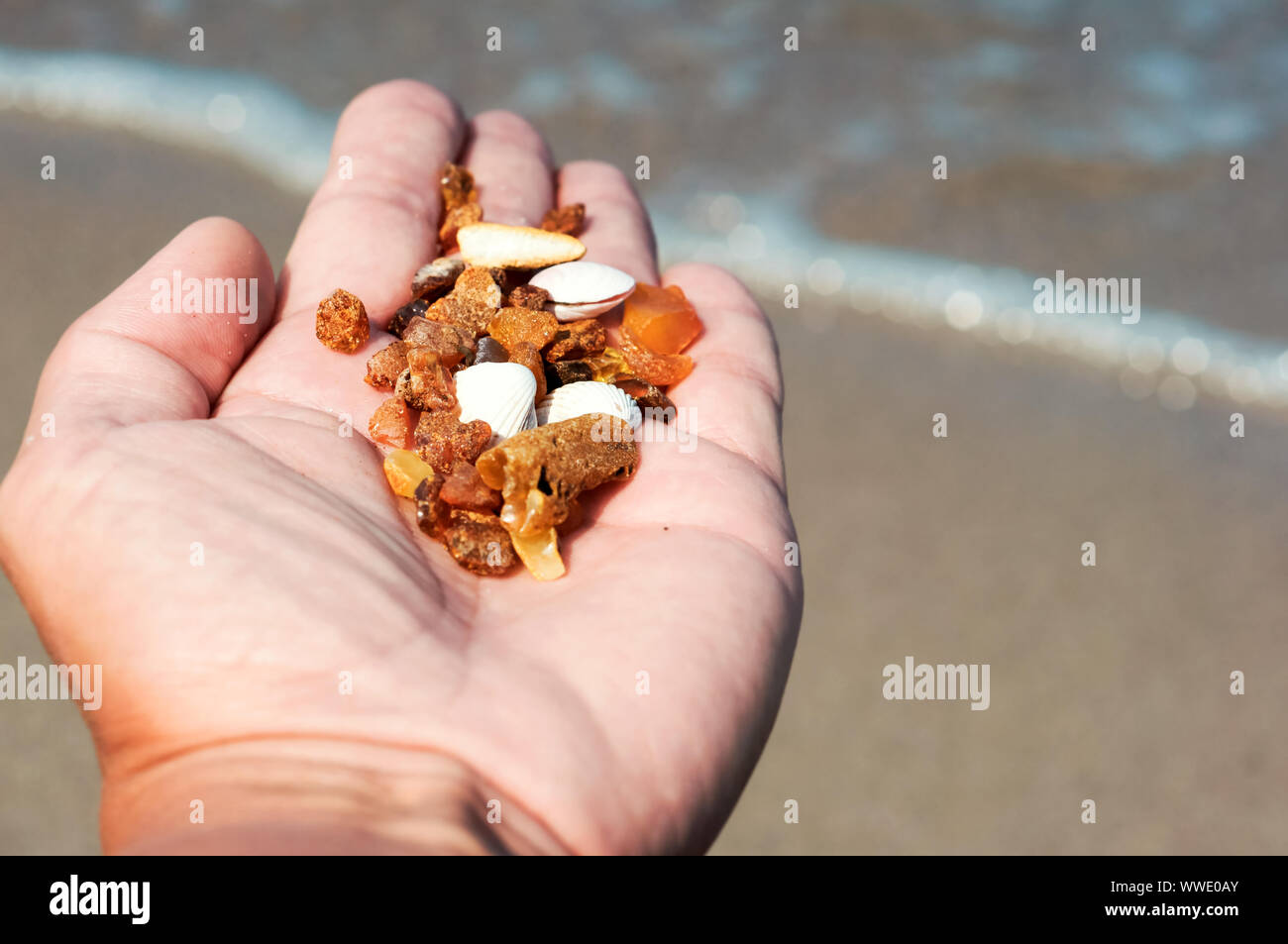 Beautiful pieces of amber in the hand of a girl with water on the sand  background Stock Photo - Alamy