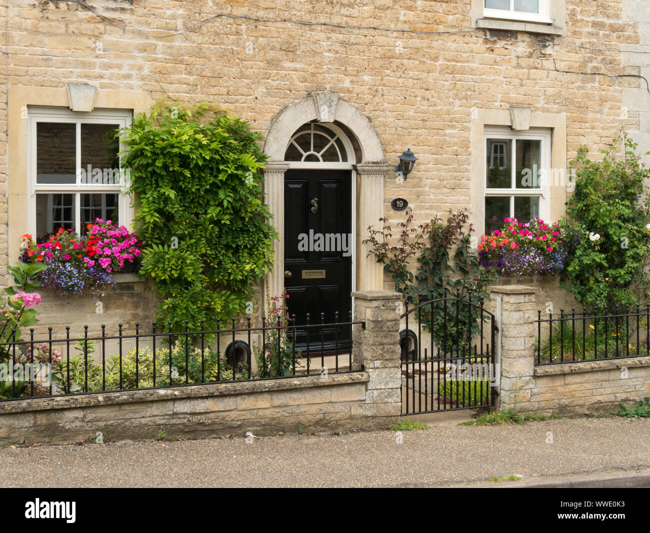 Pretty stone house with sash windows, flowering window baskets , Easton on the Hill, Northamptonshire, England, UK Stock Photo