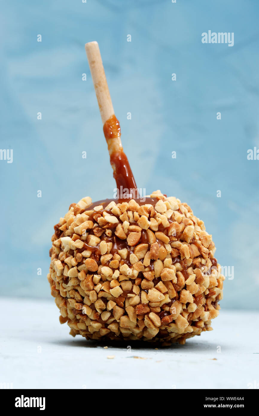 Delicious caramel apple with wood stick decorated with nuts, photographed against blue background Stock Photo