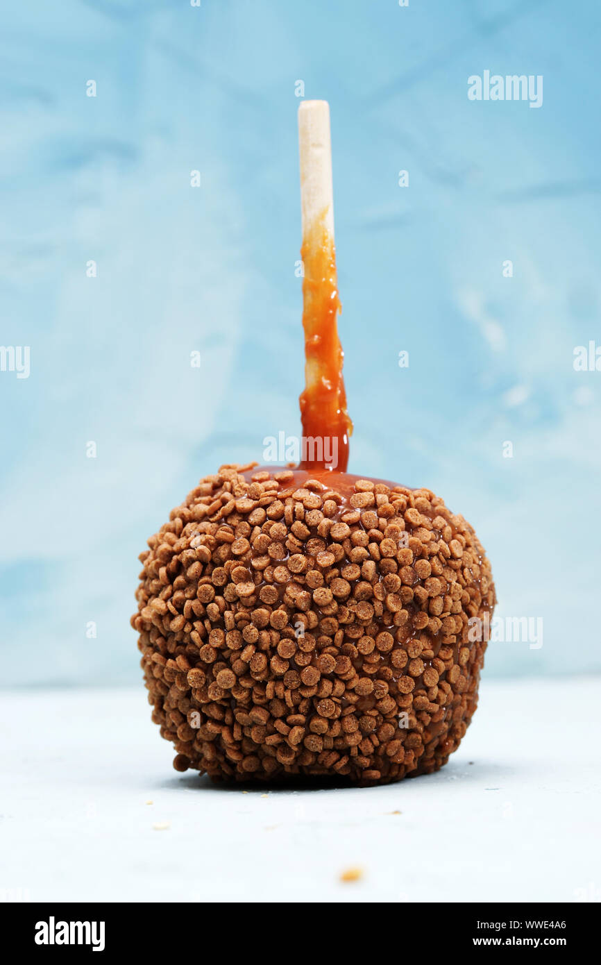 Delicious caramel apple with wood stick decorated with seeds, photographed against blue background Stock Photo