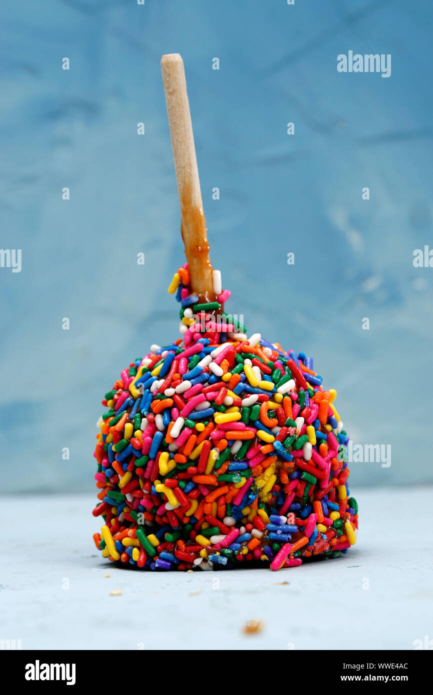 Delicious caramel apple with wood stick decorated with candy, photographed against blue background Stock Photo