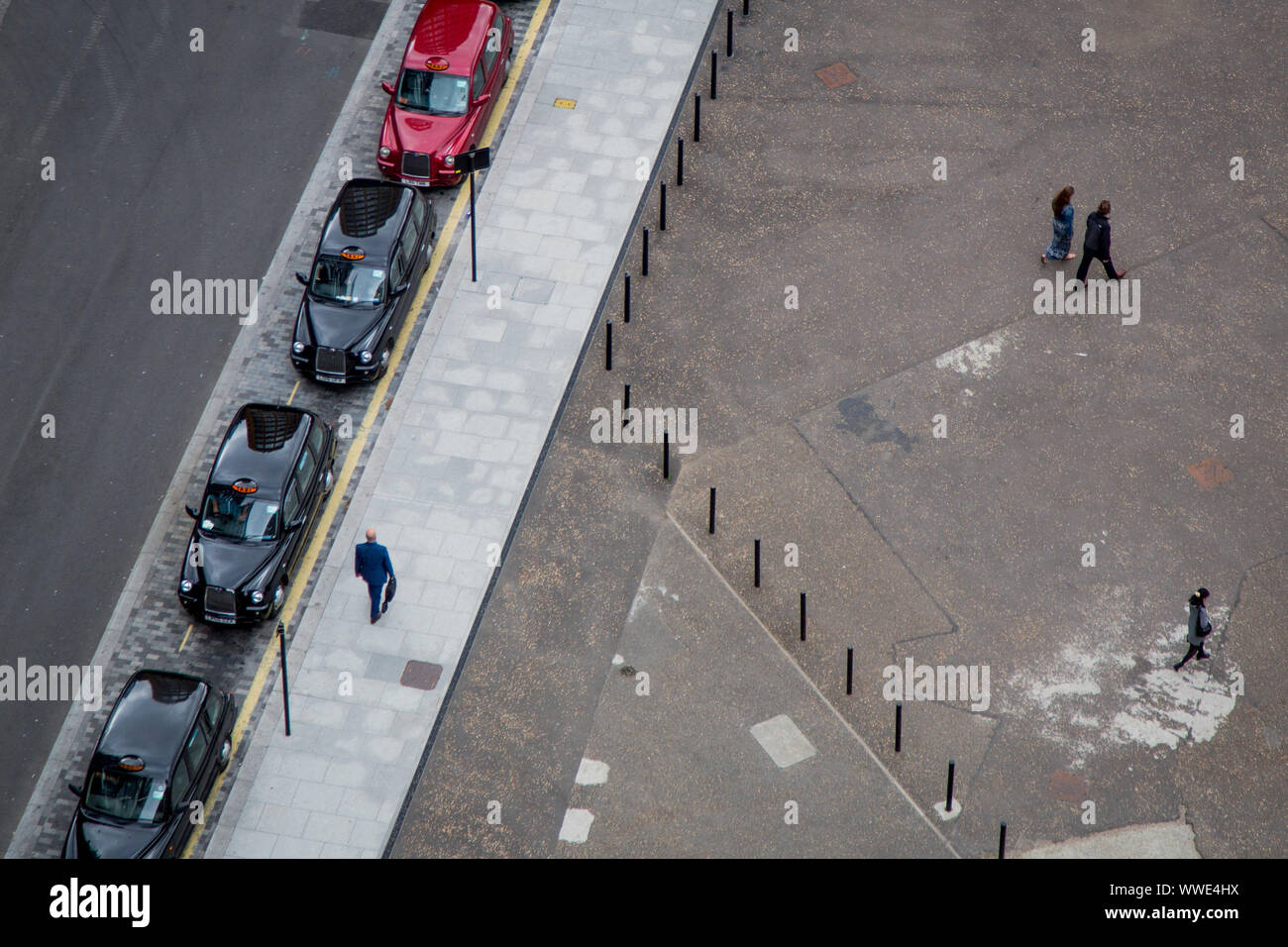 Three black London cabs and one red parked outside Tate Modern in London. Pedestrians crossing the plaza Stock Photo