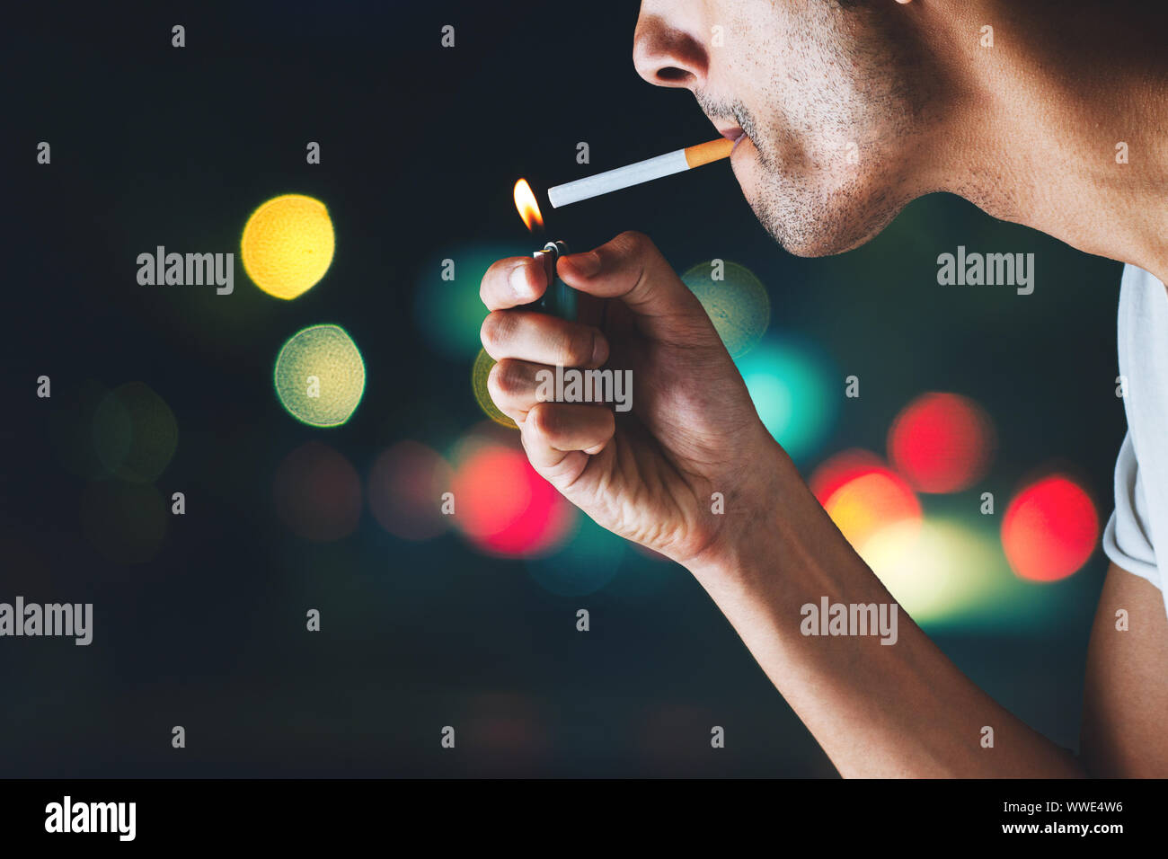 close-up of a man lighting a cigarette outside with bokeh in the background Stock Photo