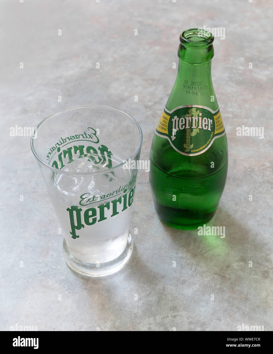 A bottle of Perrier Water and Perrier drinking glass containing ice and water. Stock Photo