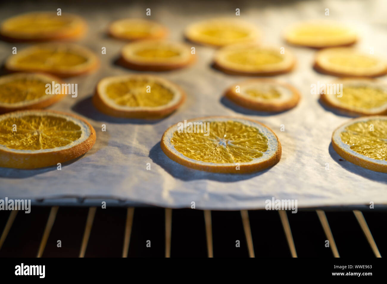 Oranges drying in the oven on a metal rack and baking paper. Selective focus on dried orange. Close up. Stock Photo