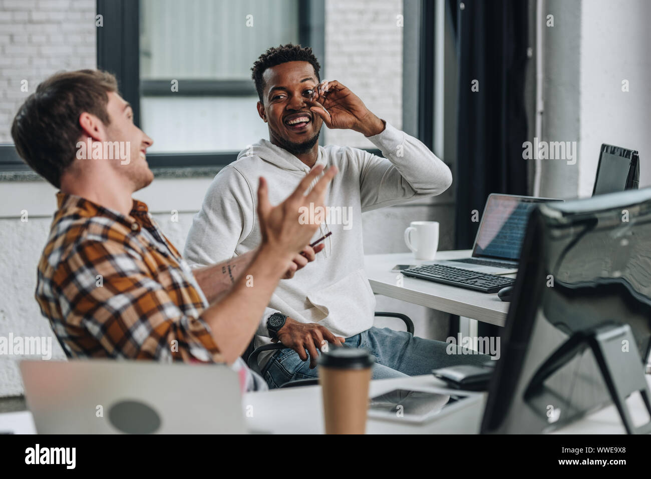 two cheerful multicultural programmers looking at each other while working in office together Stock Photo