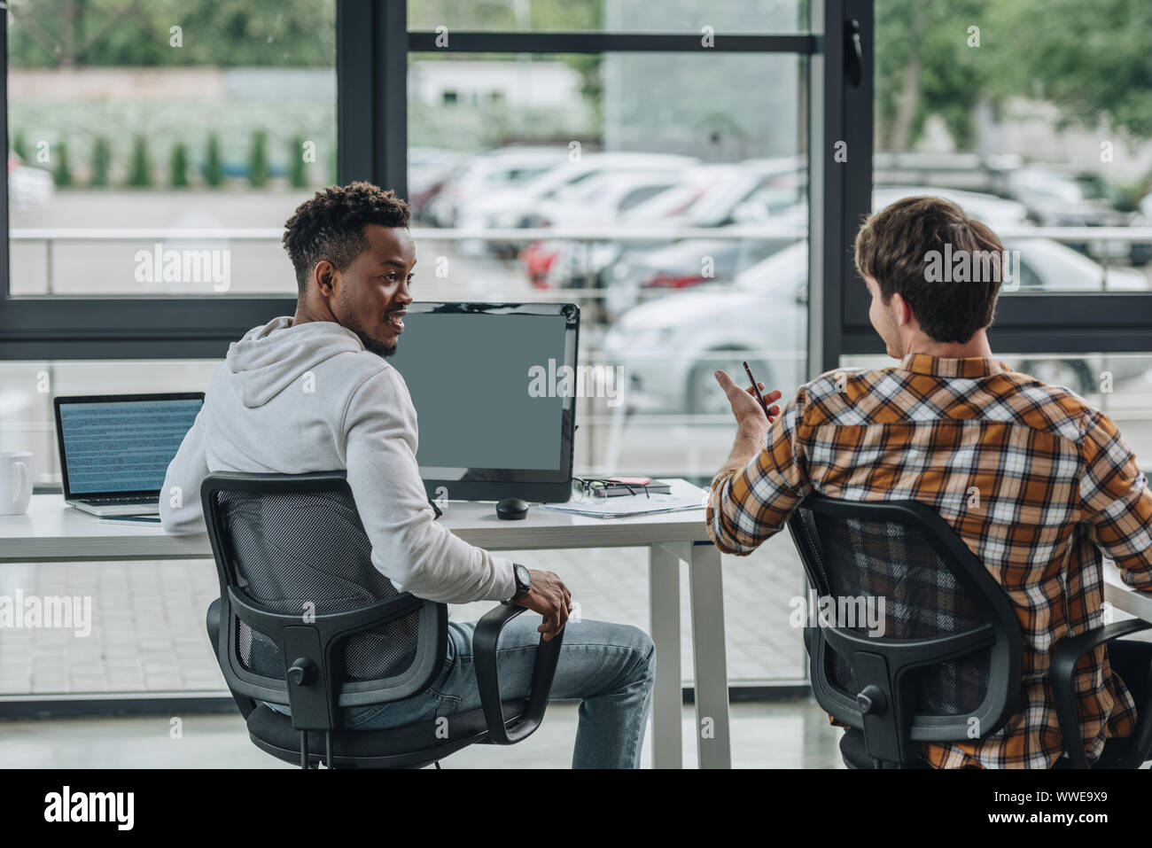 back view of young programmer talking to african american colleague in ...