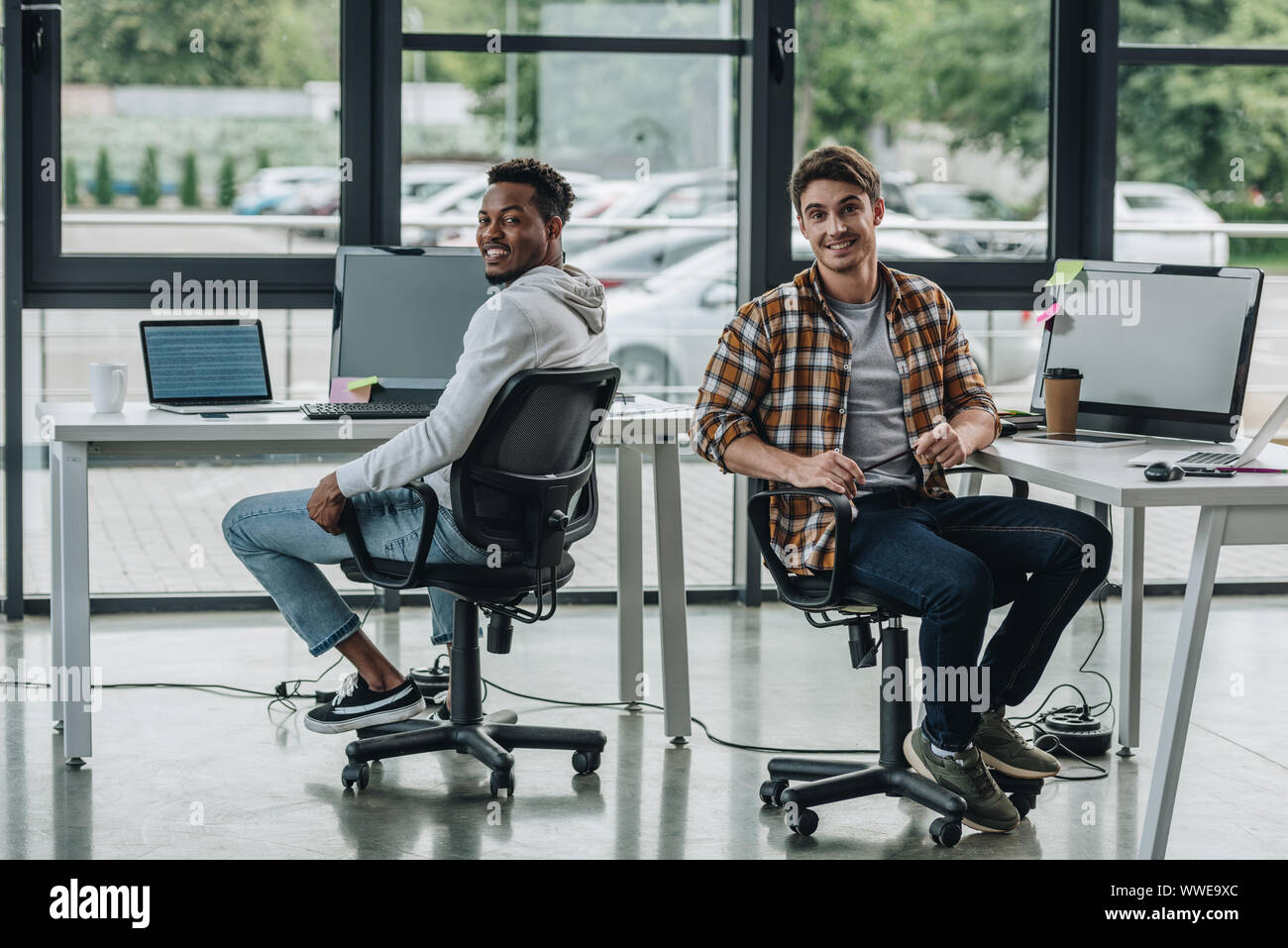 young multicultural programmers smiling at camera while sitting in