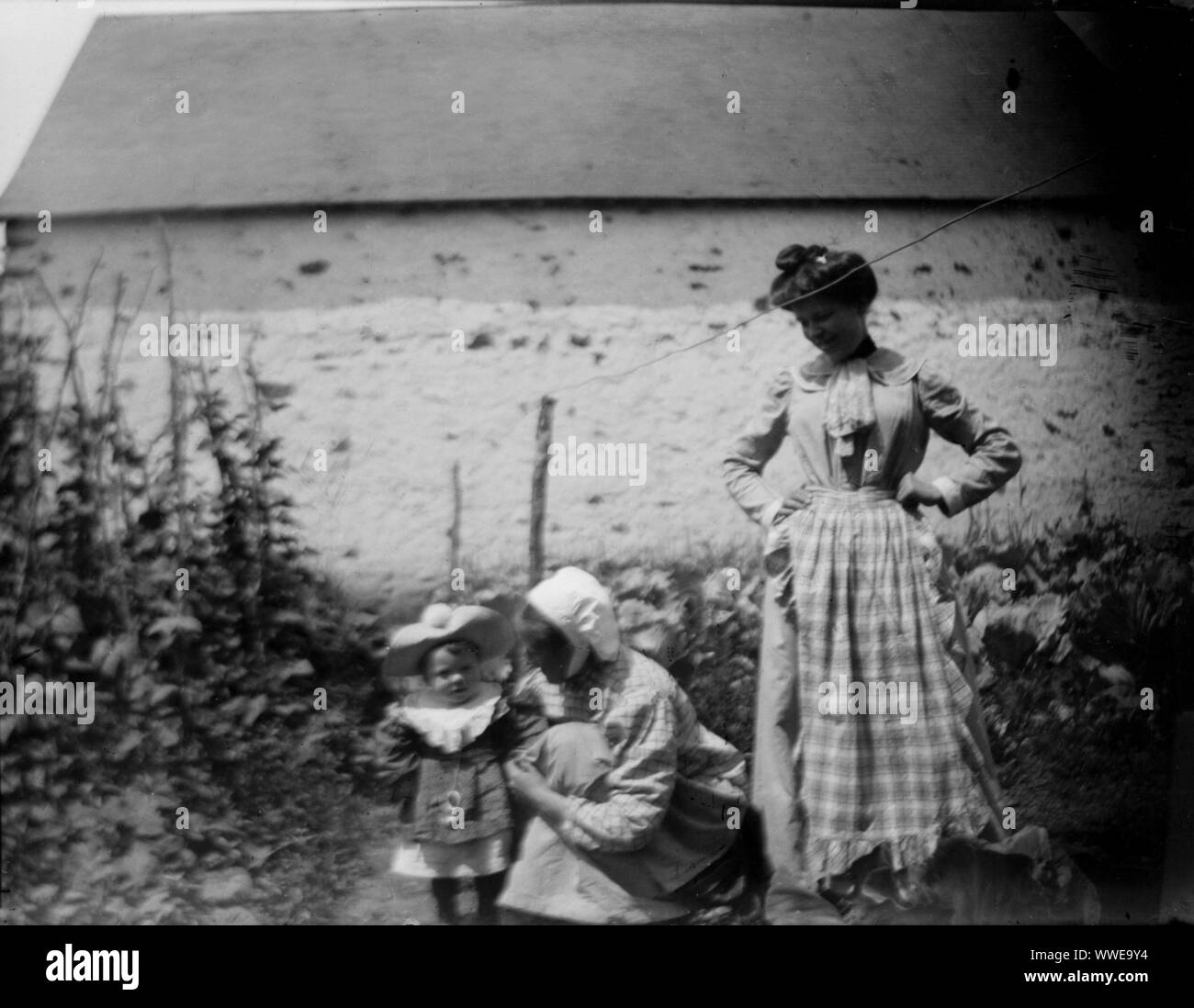 AJAXNETPHOTO. 1889-1900 (APPROX). FRANCE (EXACT LOCATION UNKNOWN.). - FAMILY SNAPSHOT - YOUNG CHILD WITH A NANNY OR MAID KNEALING, WITH A WOMAN IN CHECK DRESS LOOKING ON IN A GARDEN ENVIRONMENT. IMAGE FROM ORIGINAL GLASS PLATE NEGATIVE; DATE SOURCE FROM GLASS PLATE BOX LID.  PHOTOGRAPHER:UNKNOWN © DIGITAL IMAGE COPYRIGHT AJAX VINTAGE PICTURE LIBRARY SOURCE: AJAX VINTAGE PICTURE LIBRARY COLLECTION REF:AVL PEO FRA 1889 106 Stock Photo