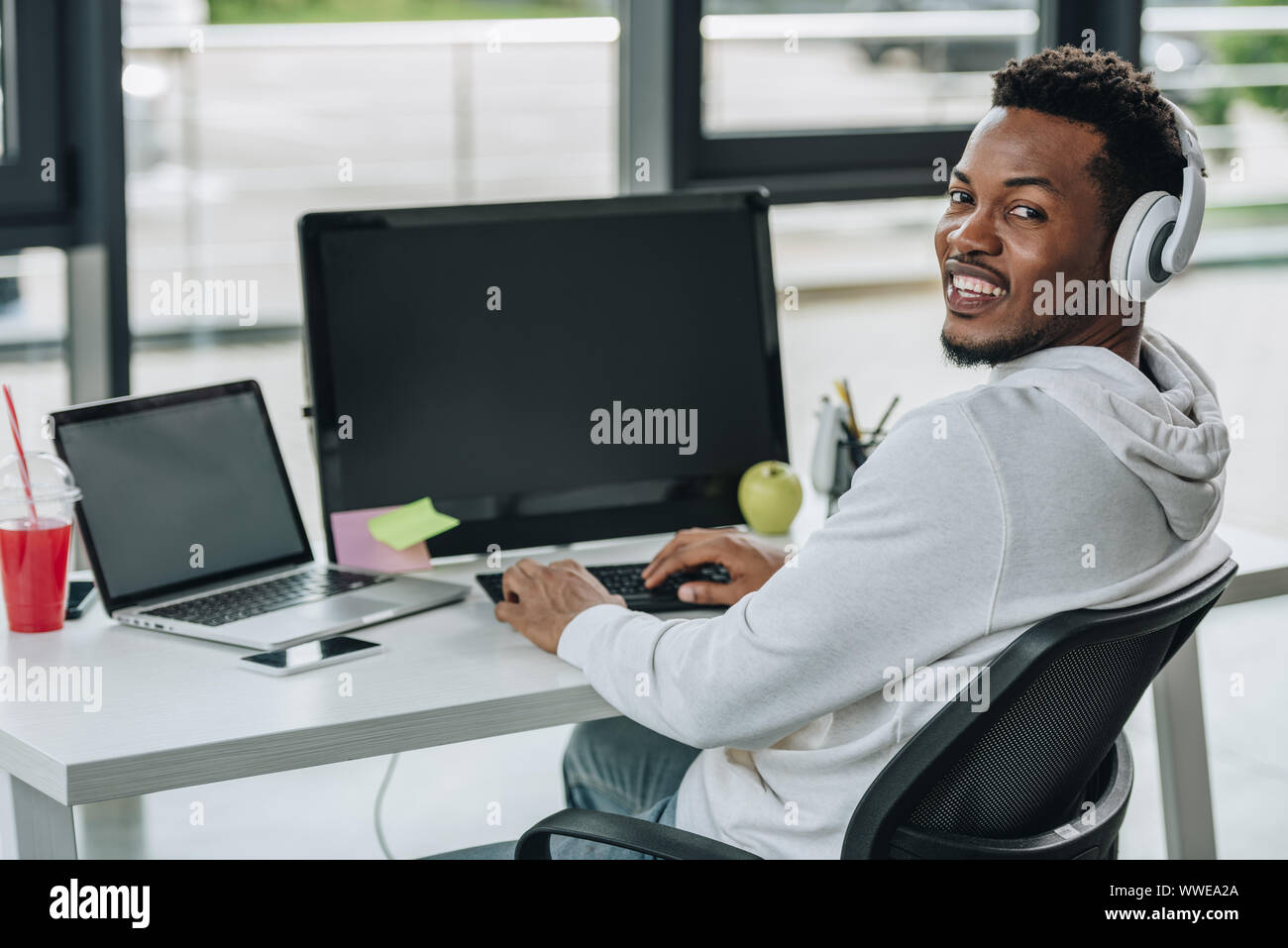 cheerful african american programmer looking at camera while sitting at workplace Stock Photo