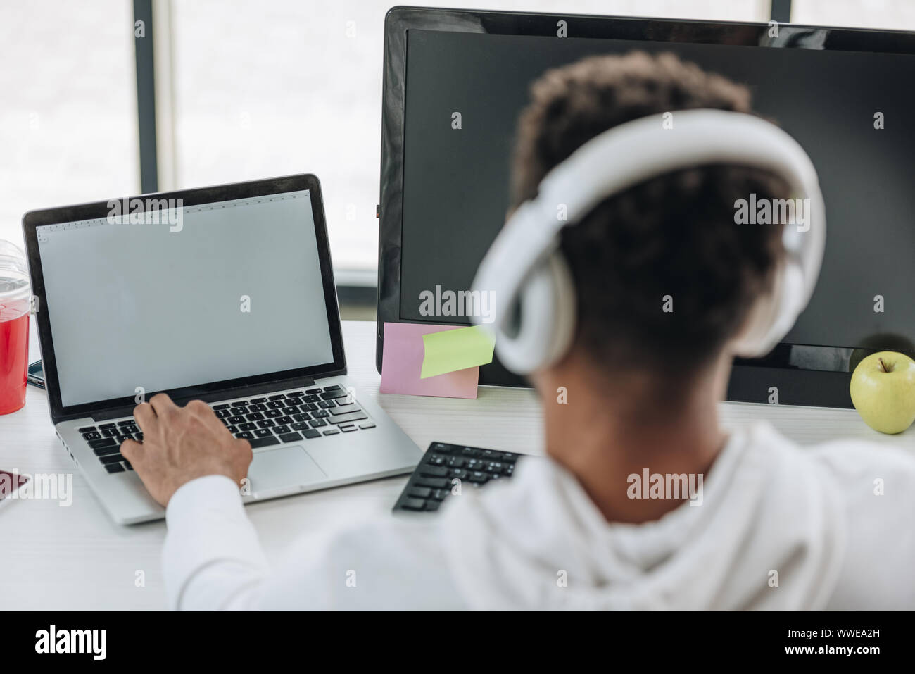 back view of african american programmer in headphones sitting at ...