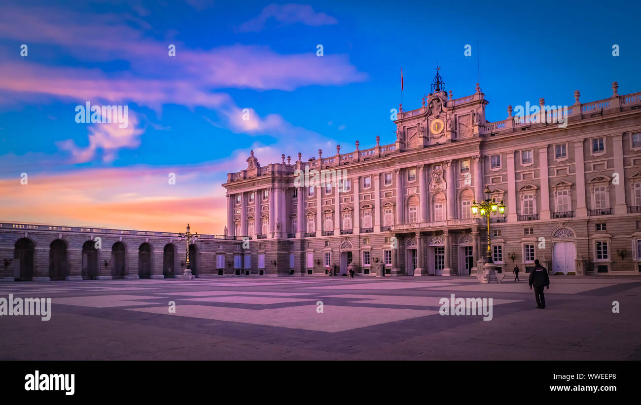 Sunset with dramatic pink sky and clouds behind the front facade of the Royal Palace from the Plaza de Armeria or Armory square in Madrid, Spain Stock Photo