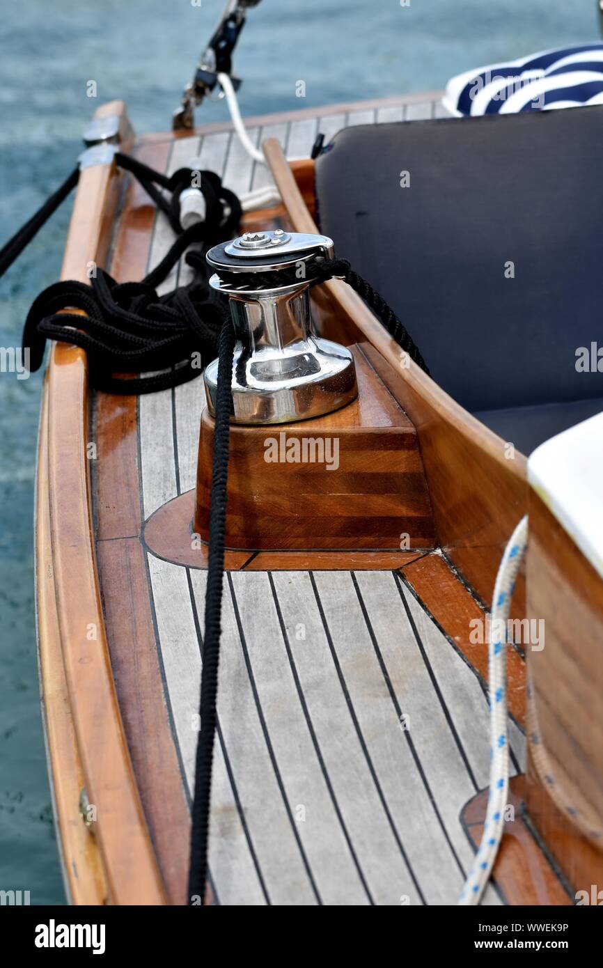 Wooden sailboat moored at the marina. Details of a classic sailing yacht with teak deck, varnished wood, winch and ropes on blurred background Stock Photo