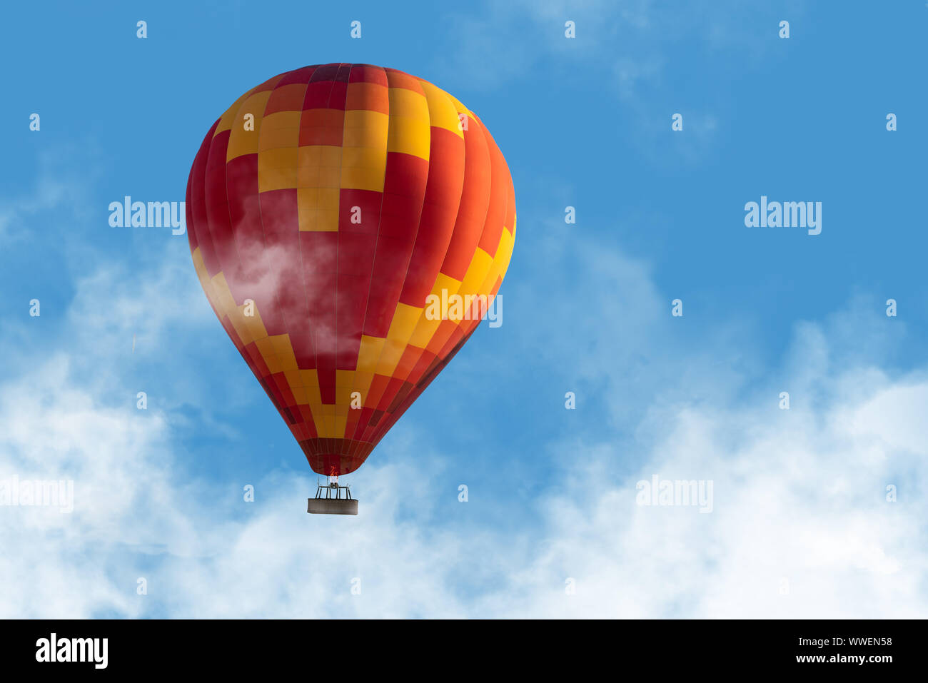 Hot air ballon floating through the clouds in blue sky Stock Photo