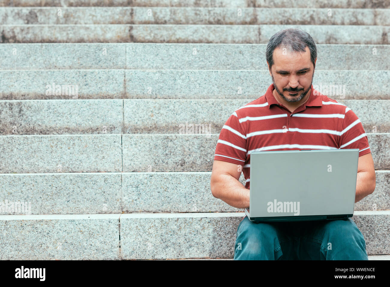 man sitting on staircase outside and working on laptop. Stock Photo