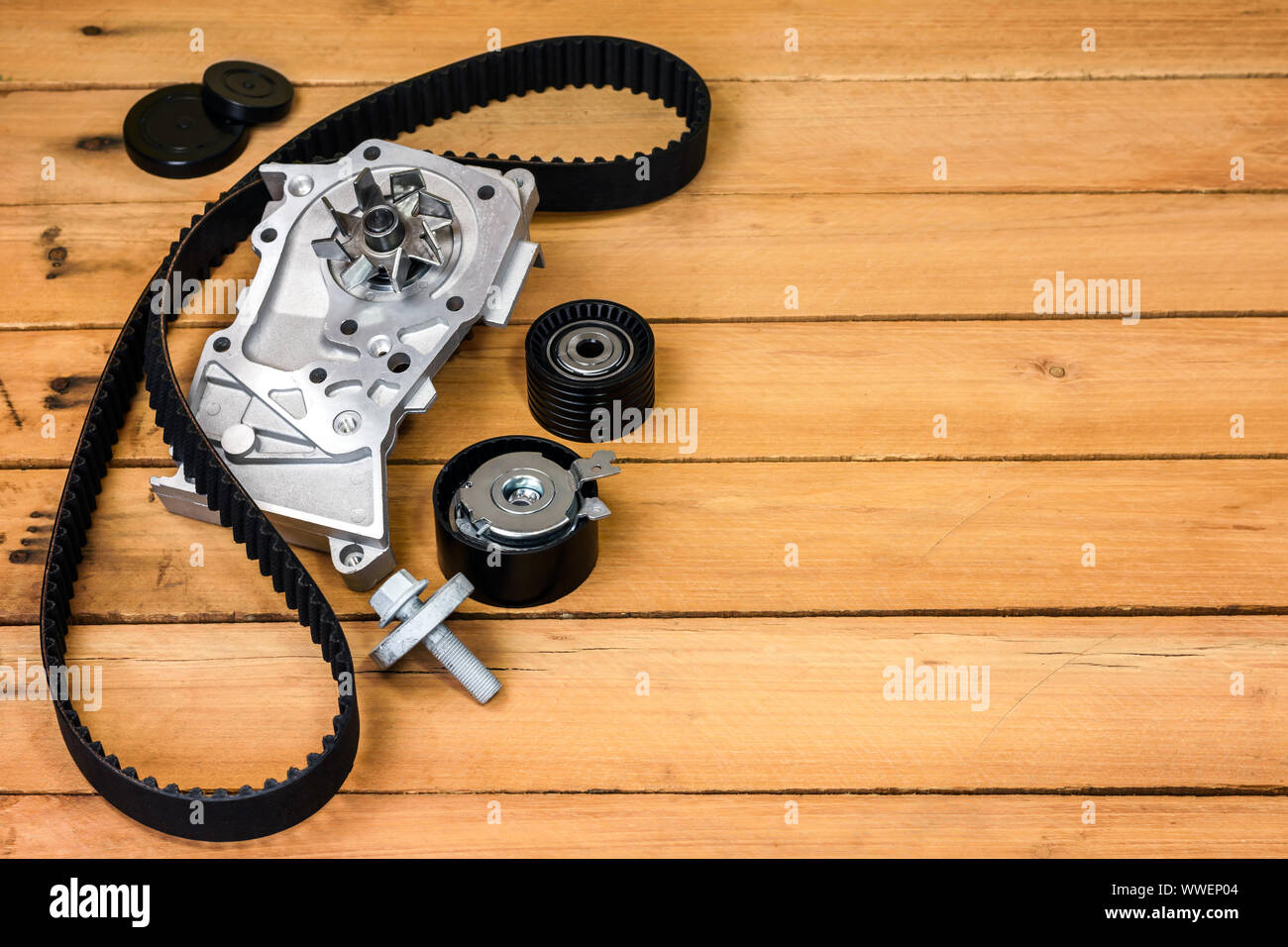 Spare parts for the car. The set of timing belt with rollers and cooling pump on a wooden background with free space for text. Stock Photo