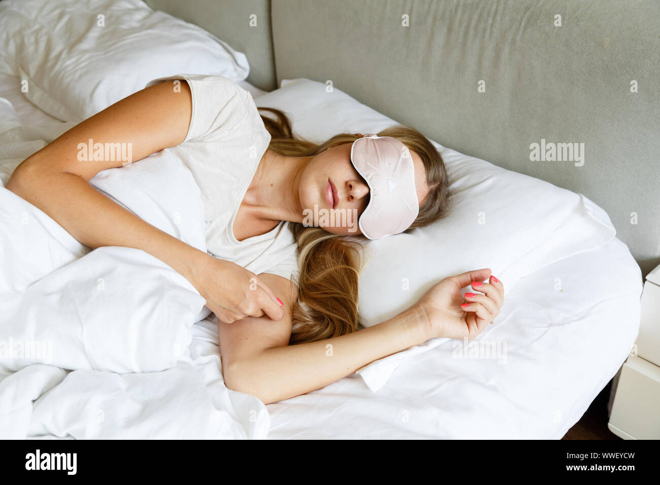 Young woman with long blonde hair sleeps on comfortable bed in a mask