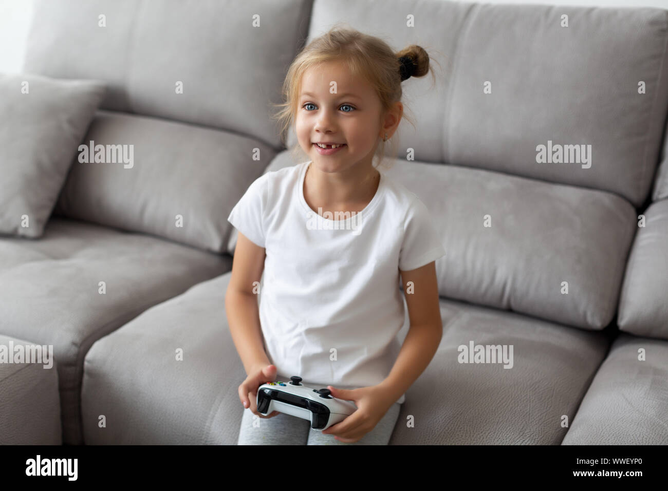 funny blonde girl without a tooth plays video games in a white t-shirt at home Stock Photo