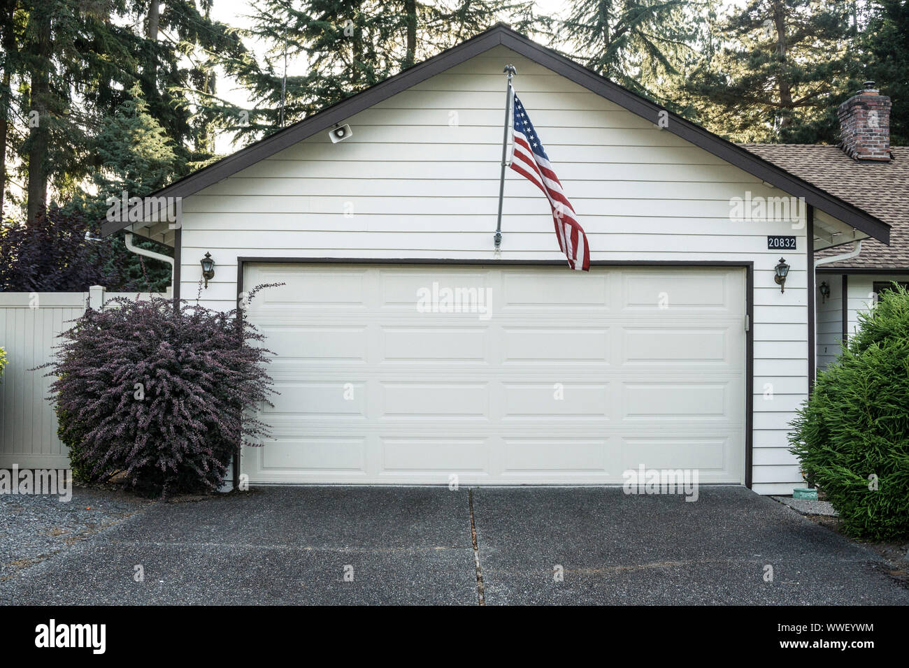 trim white suburban garage with neat horizontal wood siding trimmed in dark brown with American flag centered above the door waving in a light breeze Stock Photo