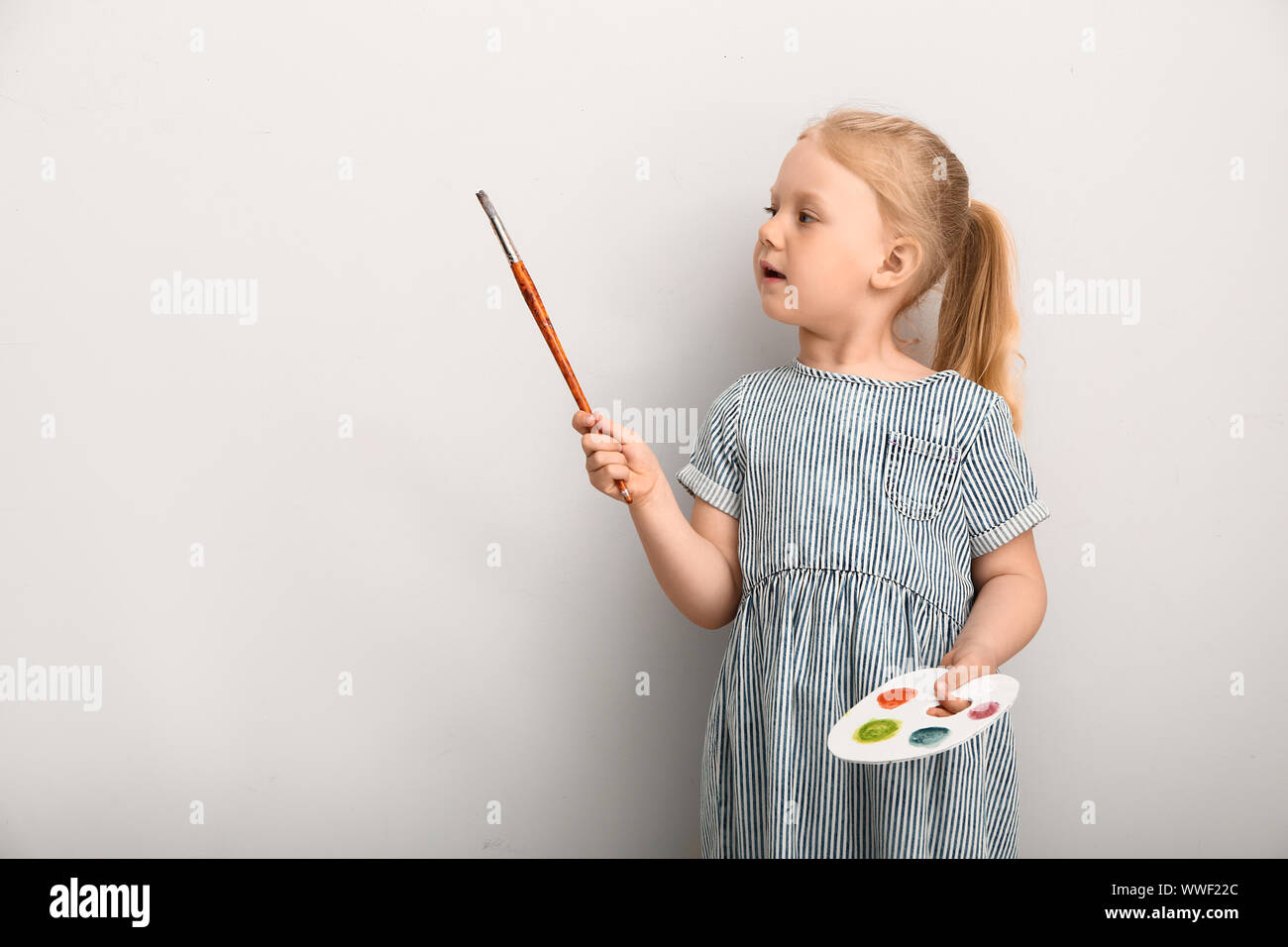 Little girl with palette and brush near light wall Stock Photo - Alamy