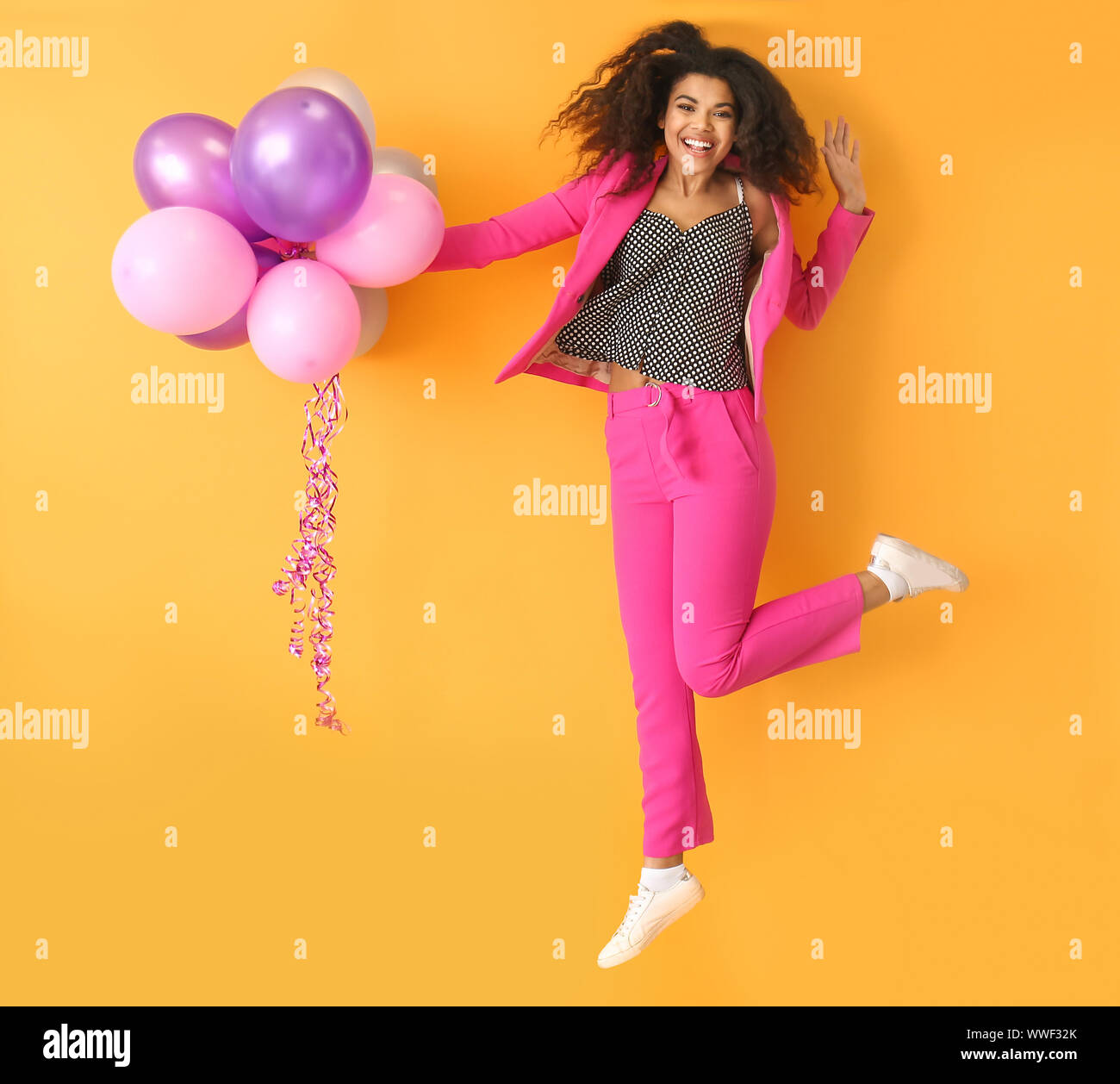 Portrait of jumping African-American woman with air balloons on color