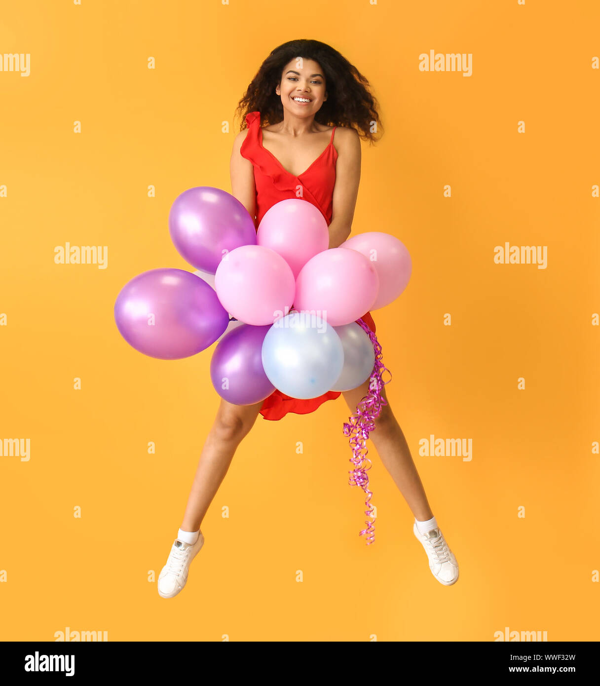 Portrait of jumping African-American woman with air balloons on color