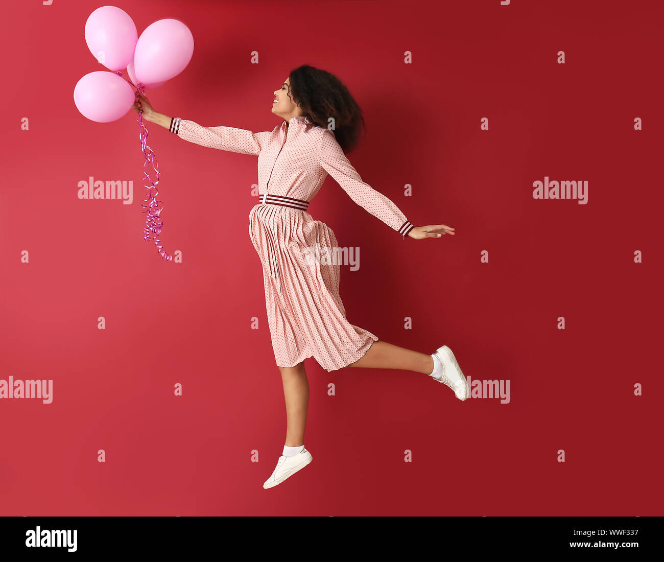 Portrait of jumping African-American woman with air balloons on color