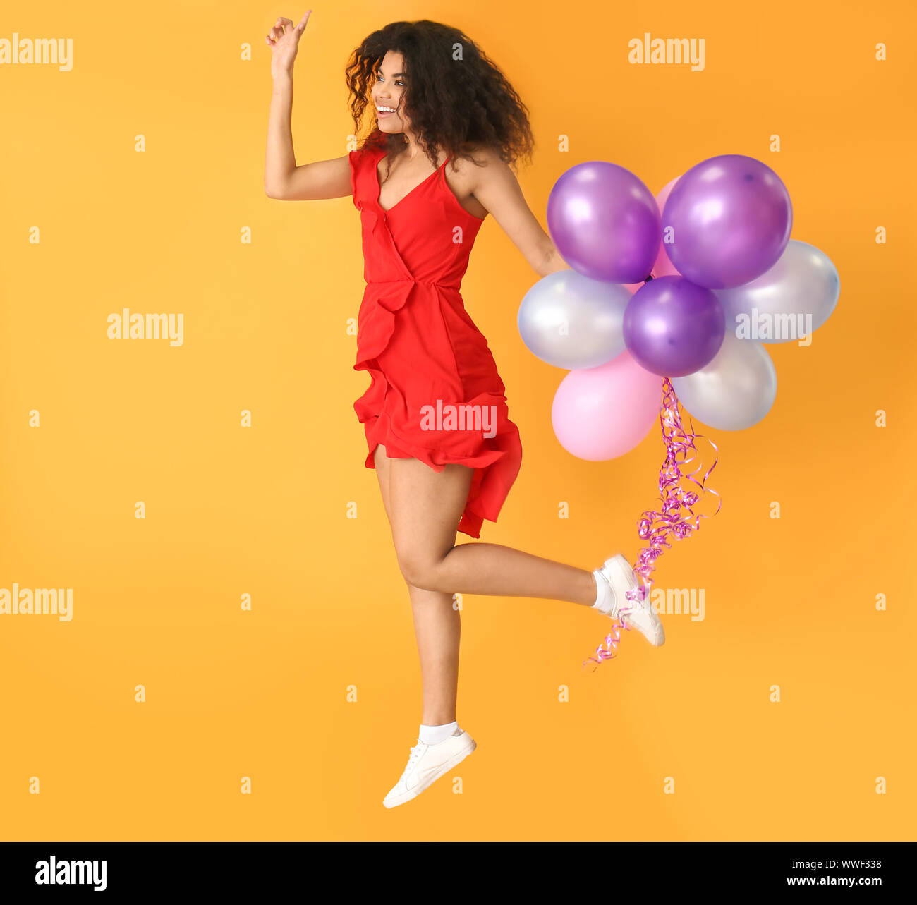 Portrait of jumping African-American woman with air balloons on color