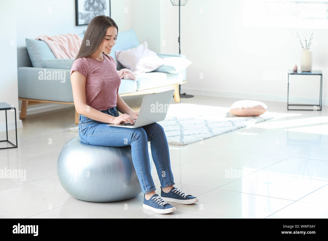 Young woman with laptop sitting on fitball at home Stock Photo - Alamy