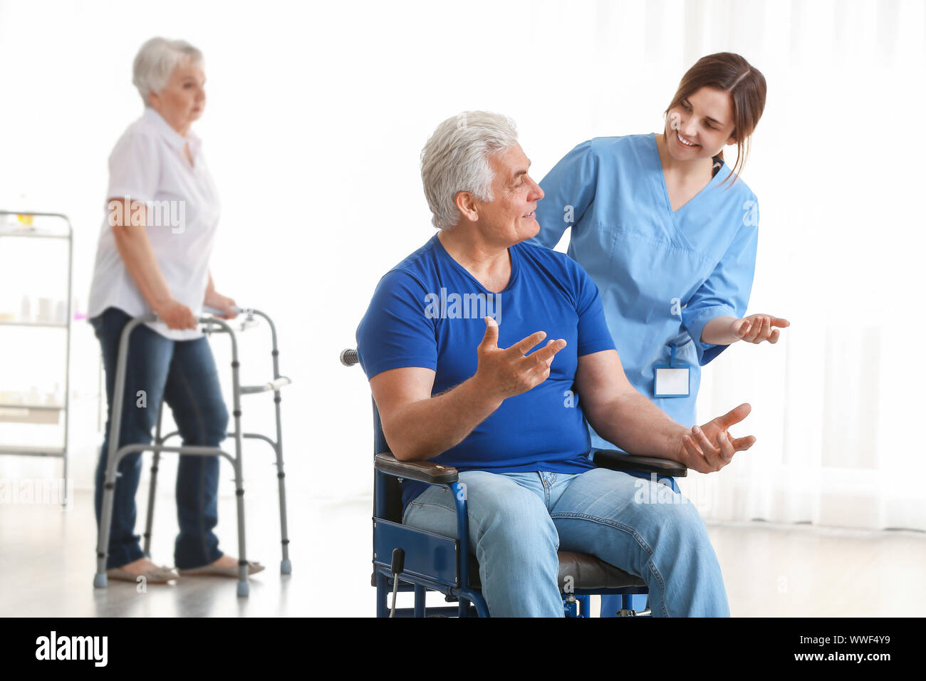Young caregiver looking after disabled mature man in nursing home Stock
