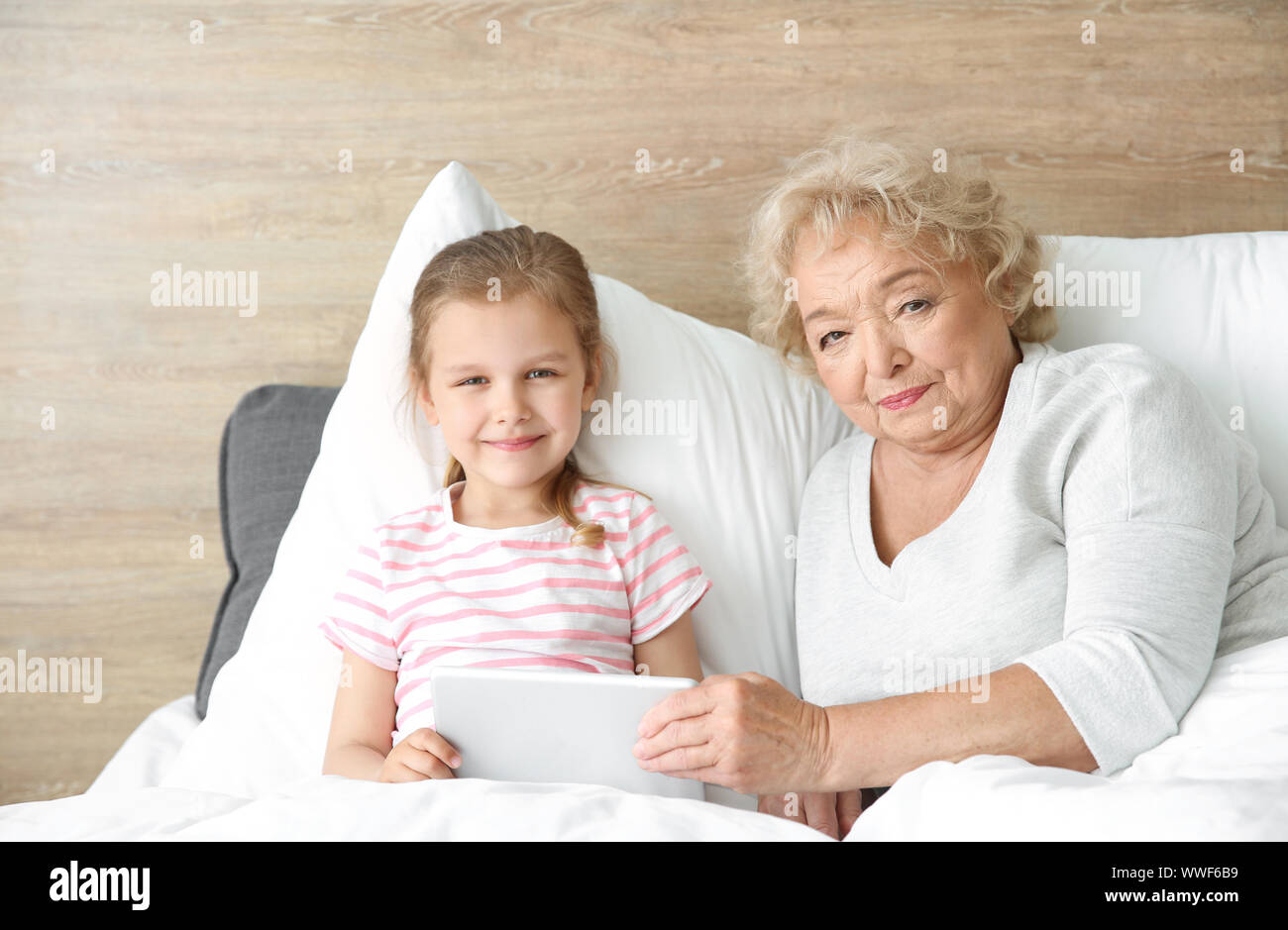 Cute little girl with grandmother using tablet PC in bed at home Stock ...