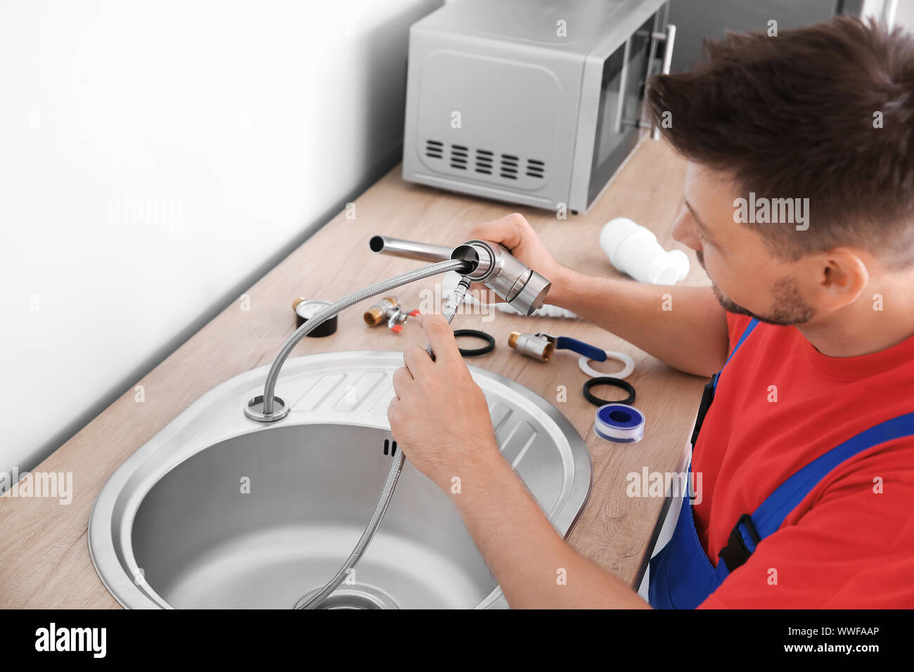 Plumber installing sink in kitchen Stock Photo