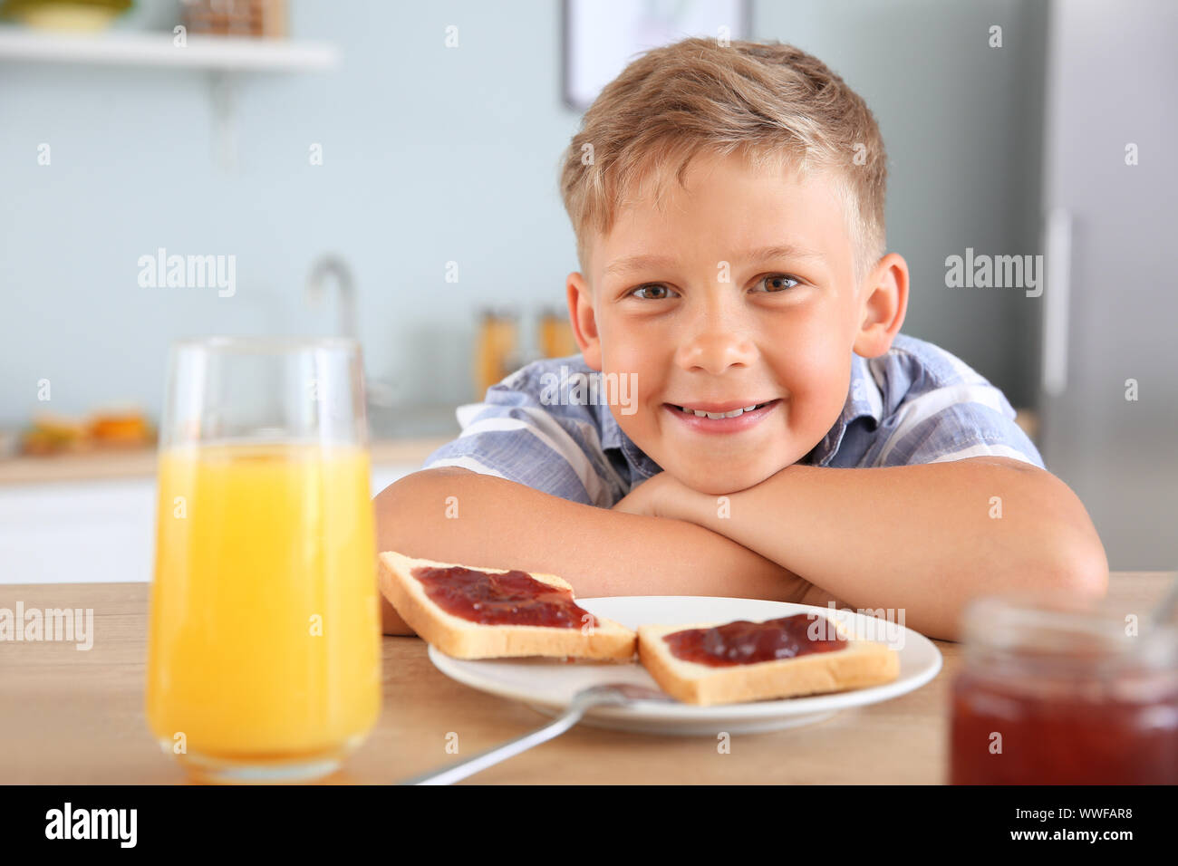 Funny little boy eating tasty toasts with jam in kitchen Stock Photo