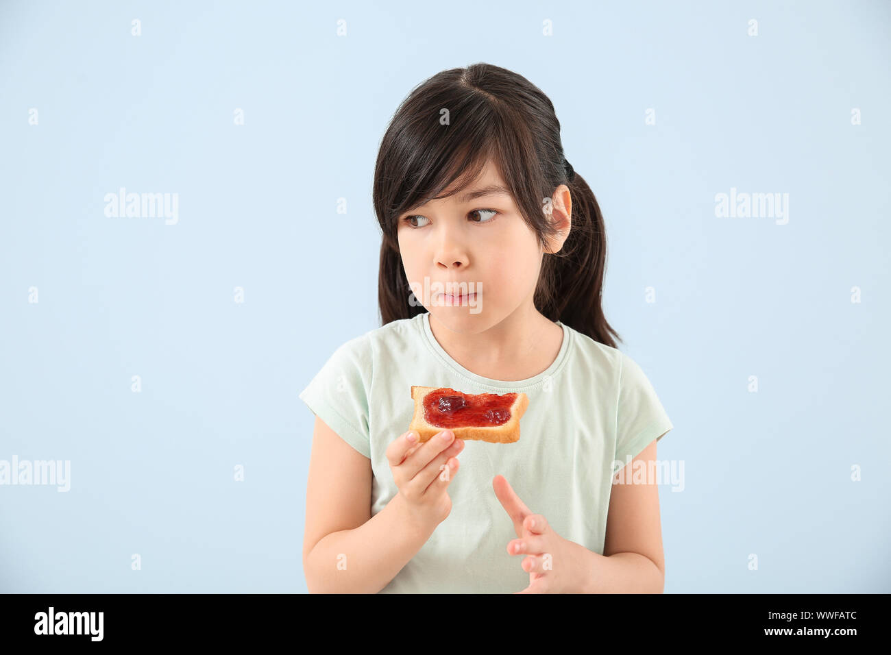 Funny little girl eating tasty toast on color background Stock Photo ...