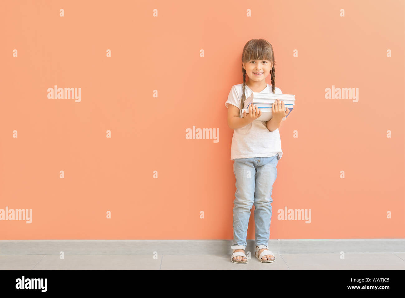 Cute little girl with books near color wall Stock Photo - Alamy